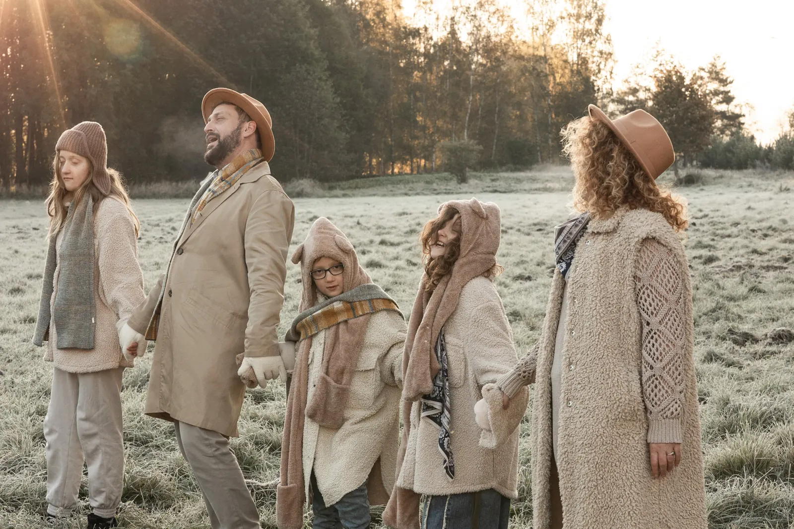 Pełna emocji fotografia rodziców z dziećmi trzymających się za ręce. W tle zimowa sceneria, mróz, łąka i las.