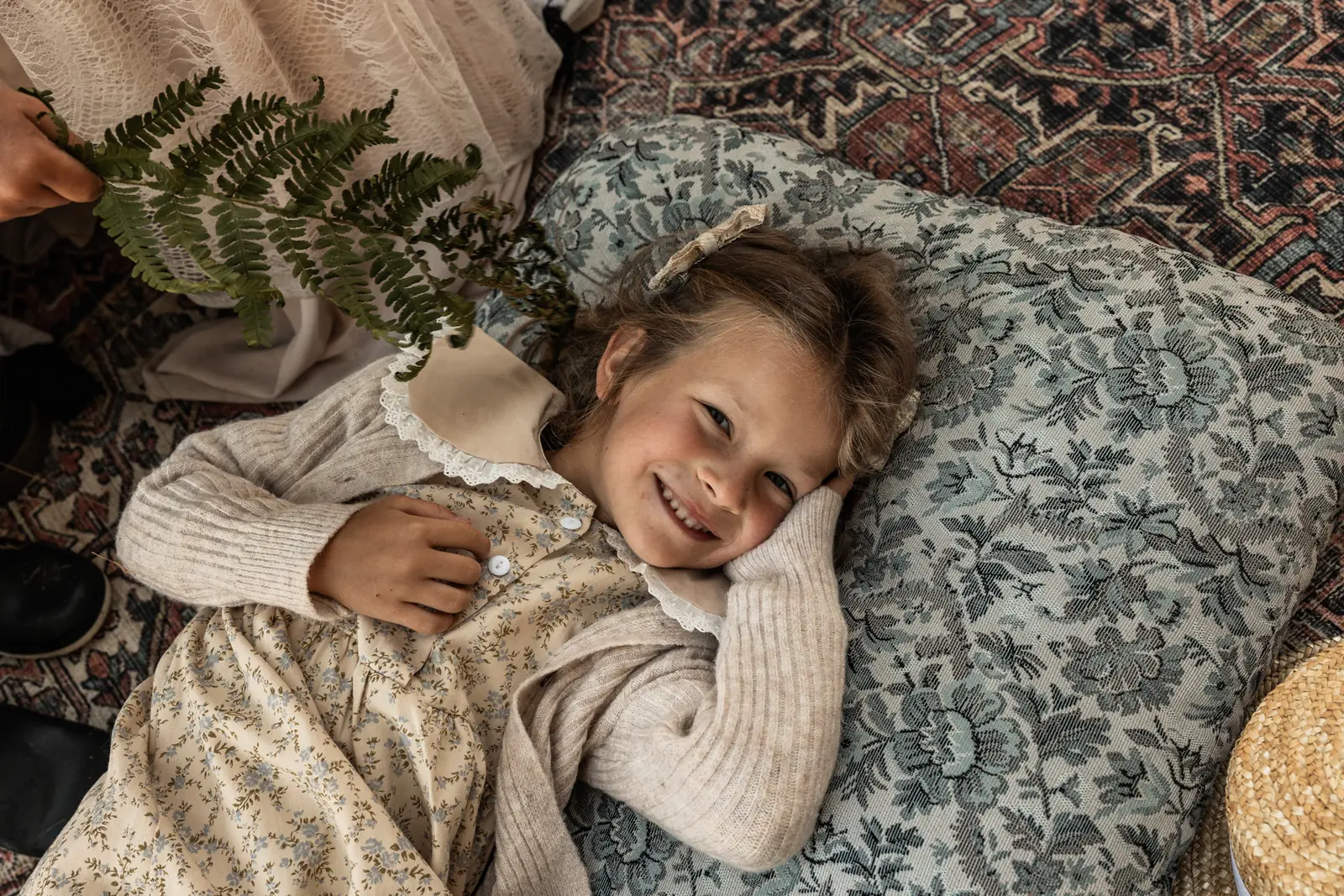 Zbliżenie na uśmiechniętą dziewczynkę leżącą na poduszce podczas sesji rodzinnej w plenerze