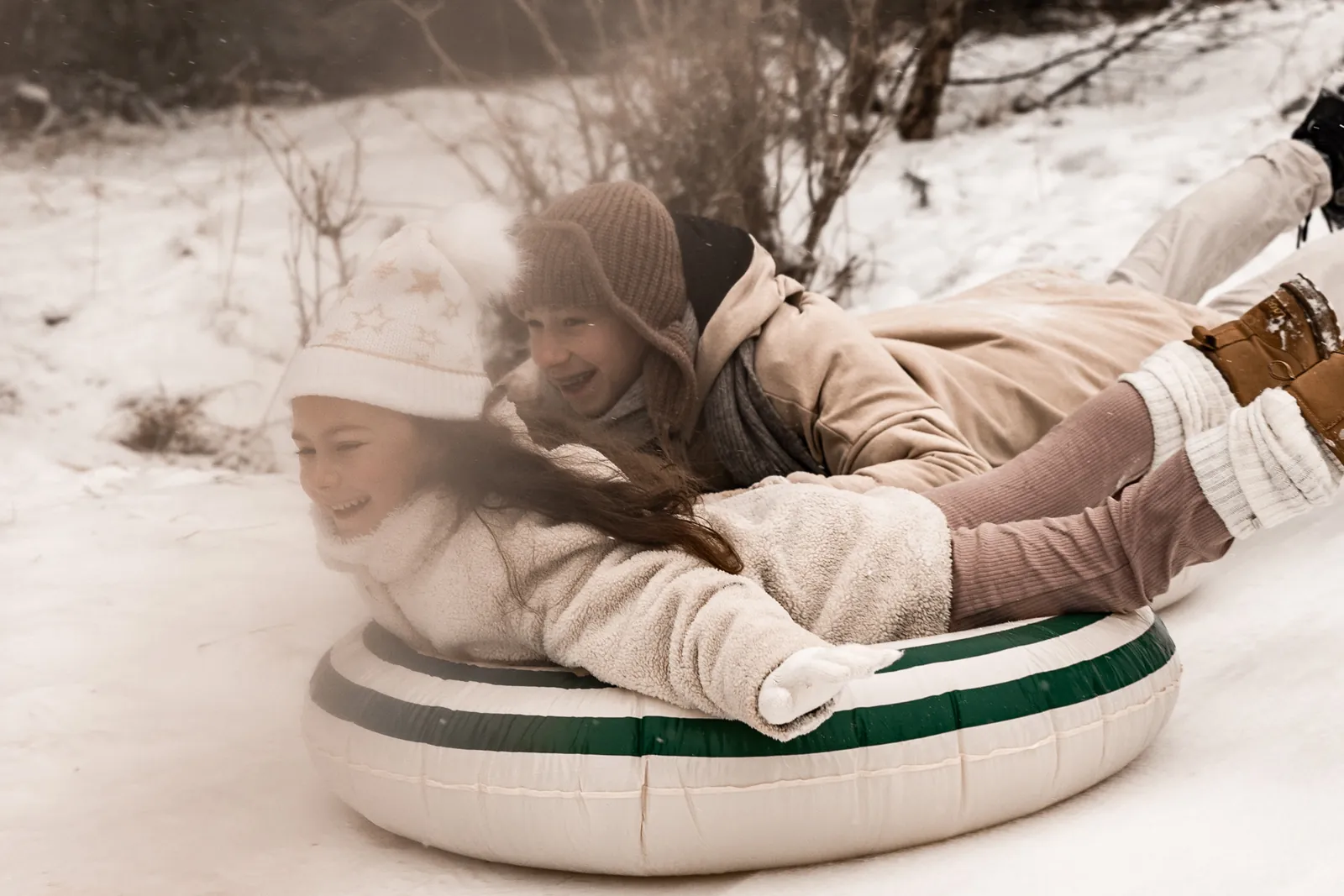 Brat i siostra ścigają się kto pierwszy zjedzie z górki na kołach po śniegu podczas sesji zdjęciowej w filmowym stylu