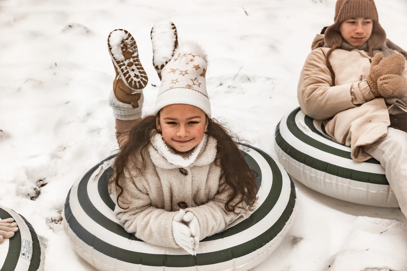 Rodzeństwo odpoczywa na dmuchanych kołach do pływania, które zastępuje im sanki w trakcie zabawy w śniegu
