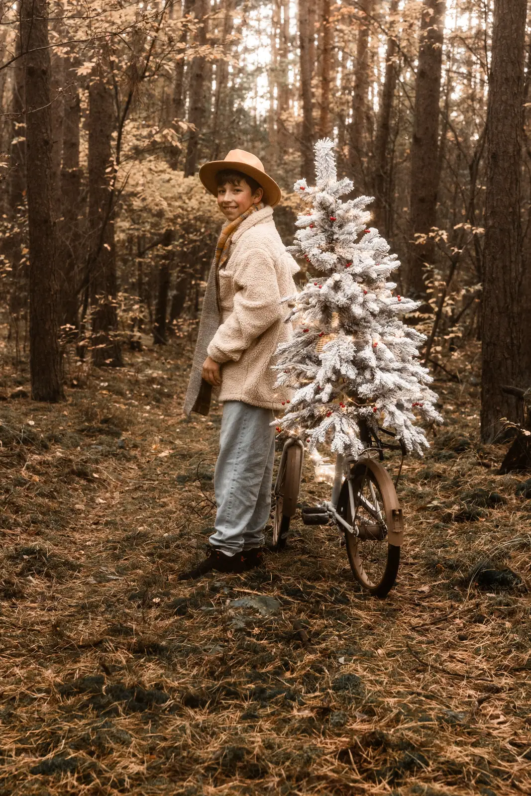 Uśmiechnięty chłopiec opiera się o rower z choinką w lesie podczas sesji świątecznej