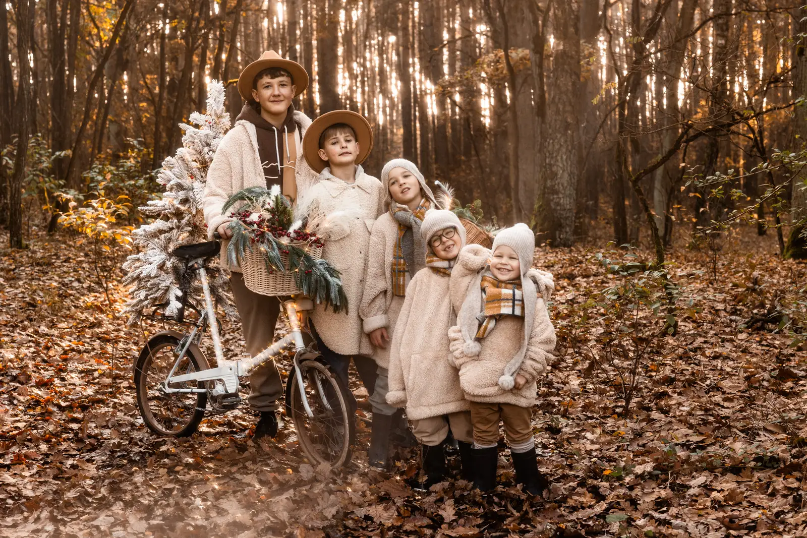 Dzieci przy choince w plenerze podczas sesji świątecznej. W tle ozdoby, drzewa i jesienne liście.