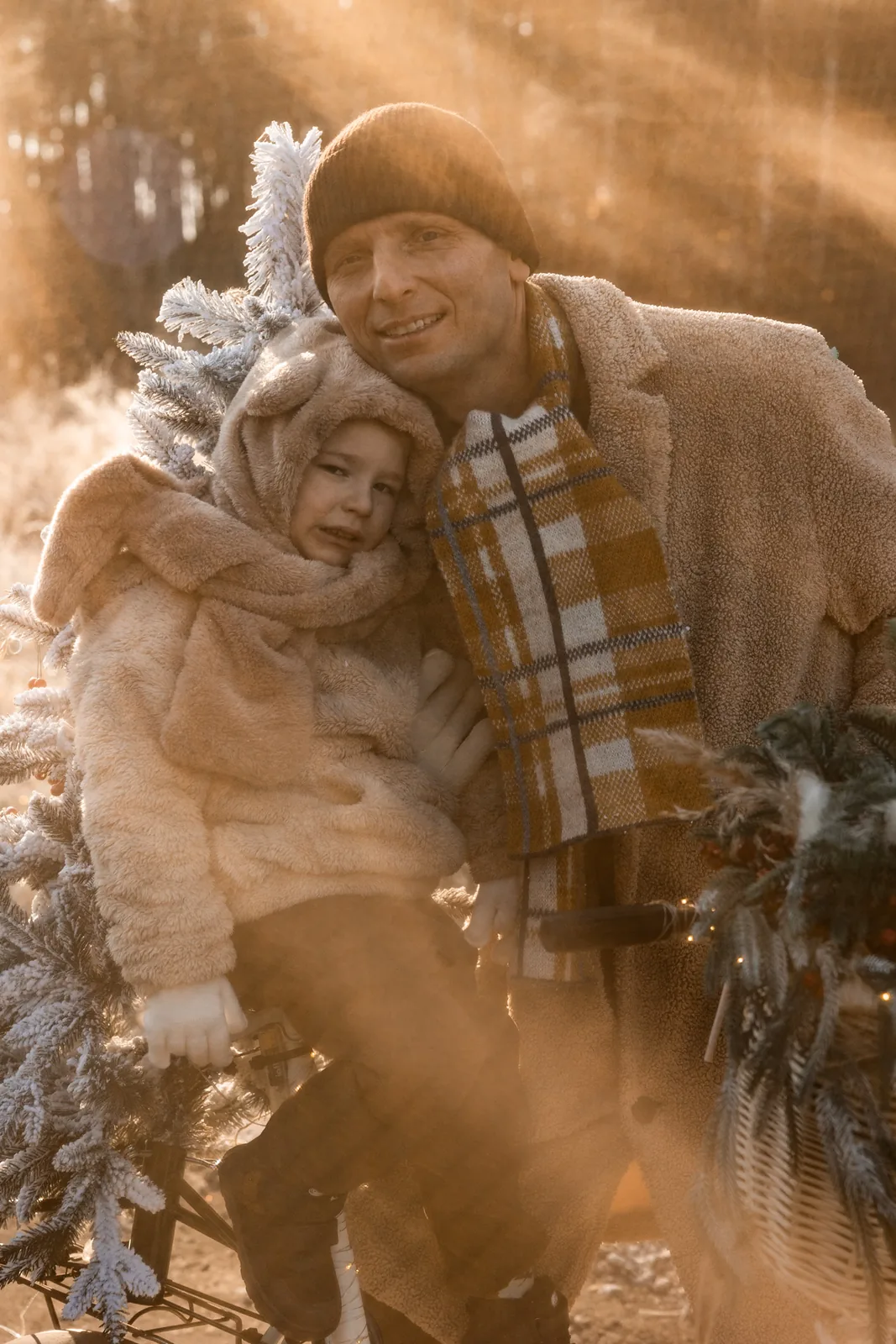Portret taty z dzieckiem podczas zimowej sesji zdjęciowej w plenerze. W tle rower z choinką.