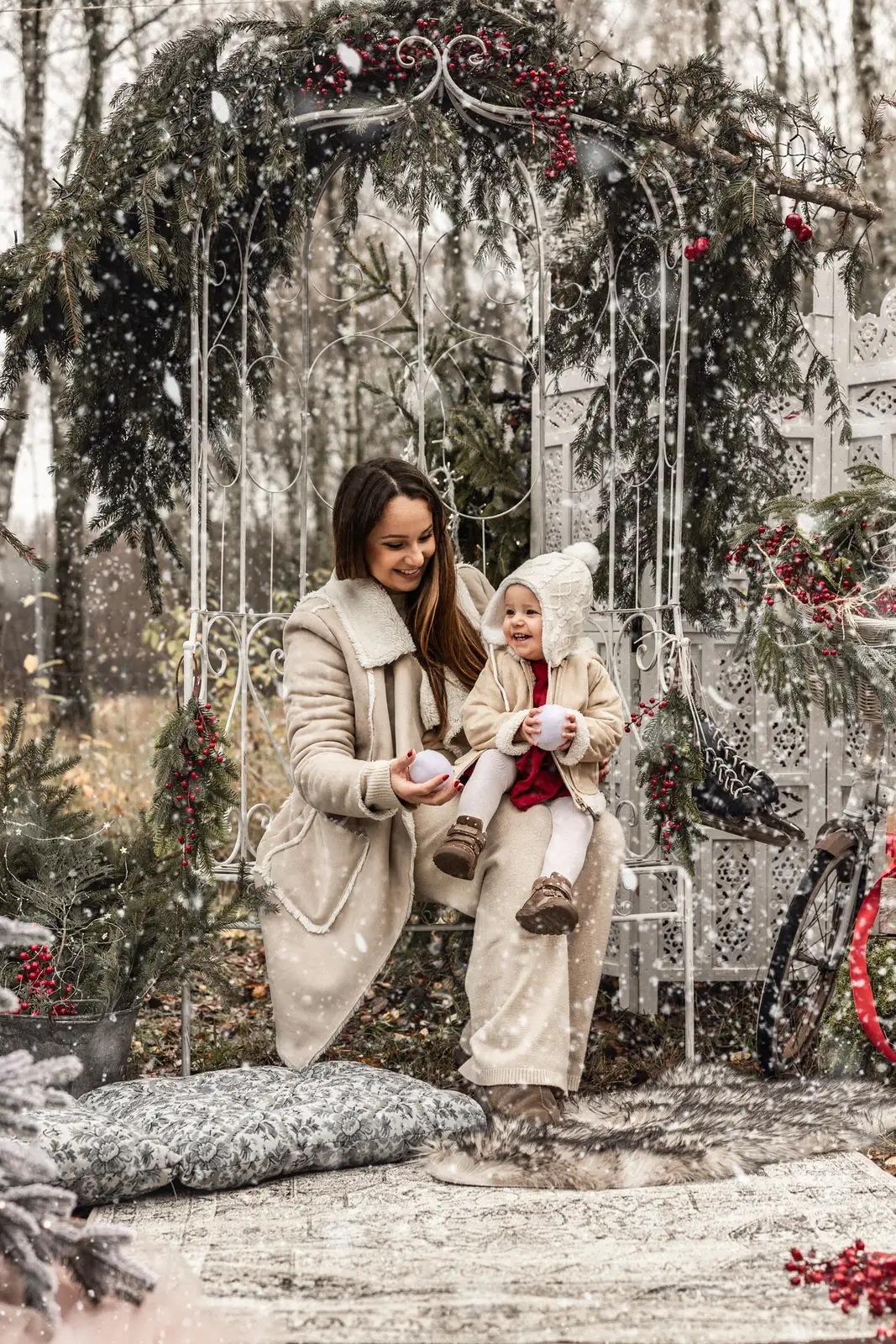 Mama z dzieckiem siedzą na ławce i bawią się śniegiem podczas zimowej sesji świątecznej