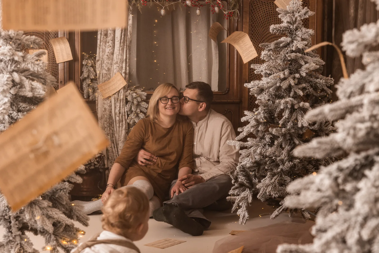 Rodzice przytuleni przy choince i retro kredensie w studio fotograficznym