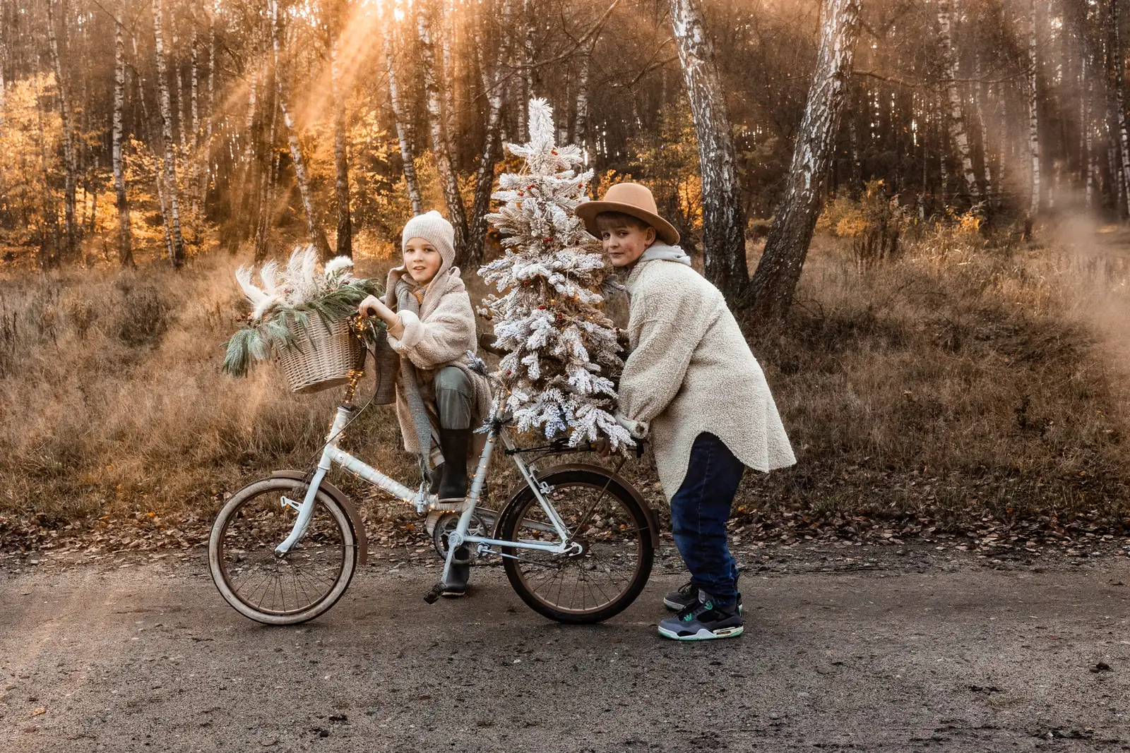 Rodzeństwo na rowerze świątecznym z choinką na bagażniku i ubranym w lampki podczas sesji bożonarodzeniowej w plenerze