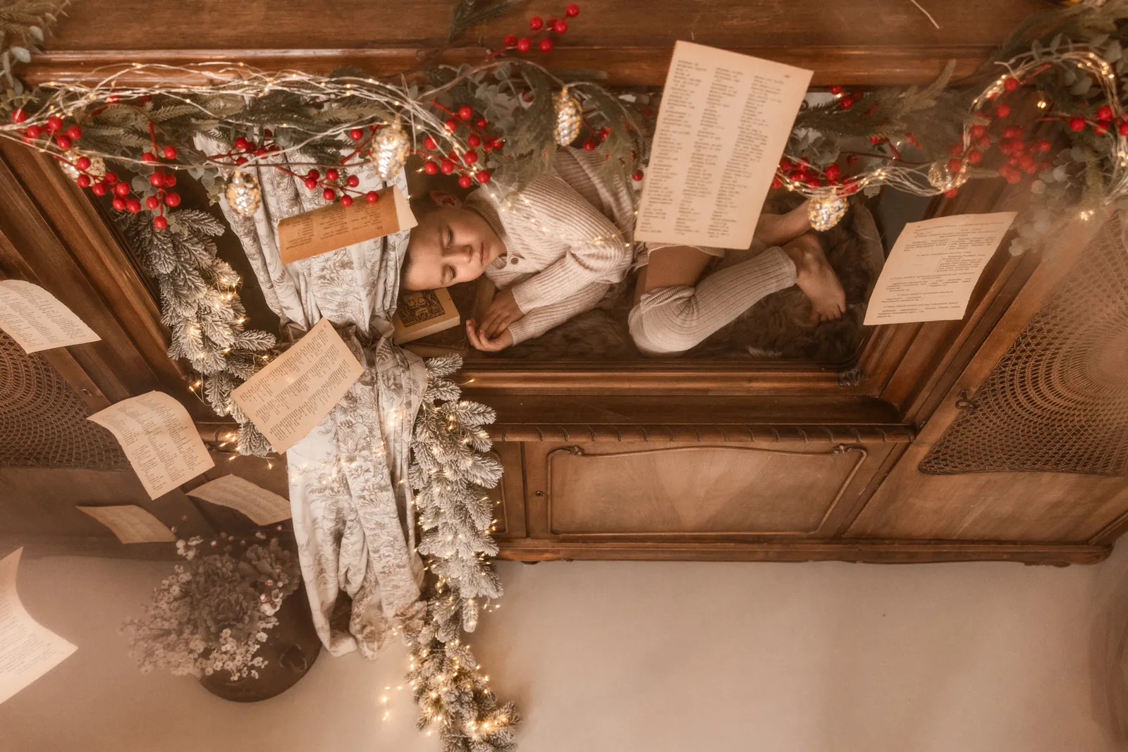 Dziecko z zamkniętymi oczami leży na stylowym kredensie ubranym w ozdoby świąteczne