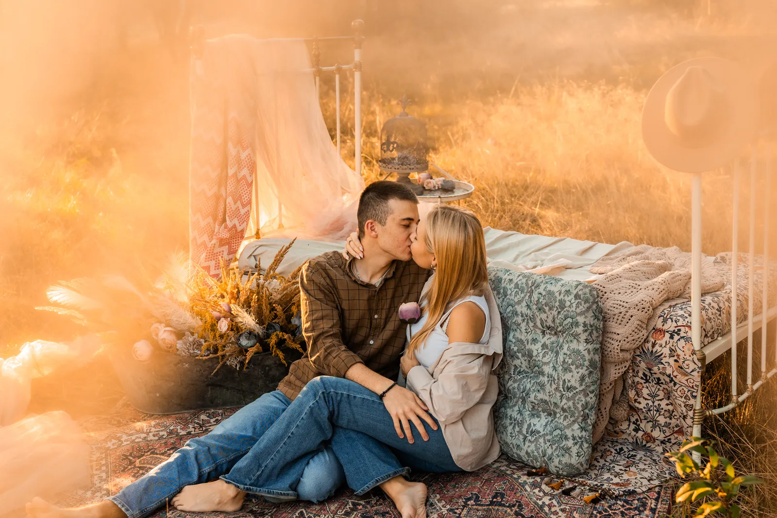 Para całuje się podczas naturalnej sesji dla par o wschodzie słońca w lesie. W tle mgła i wschód słońca.