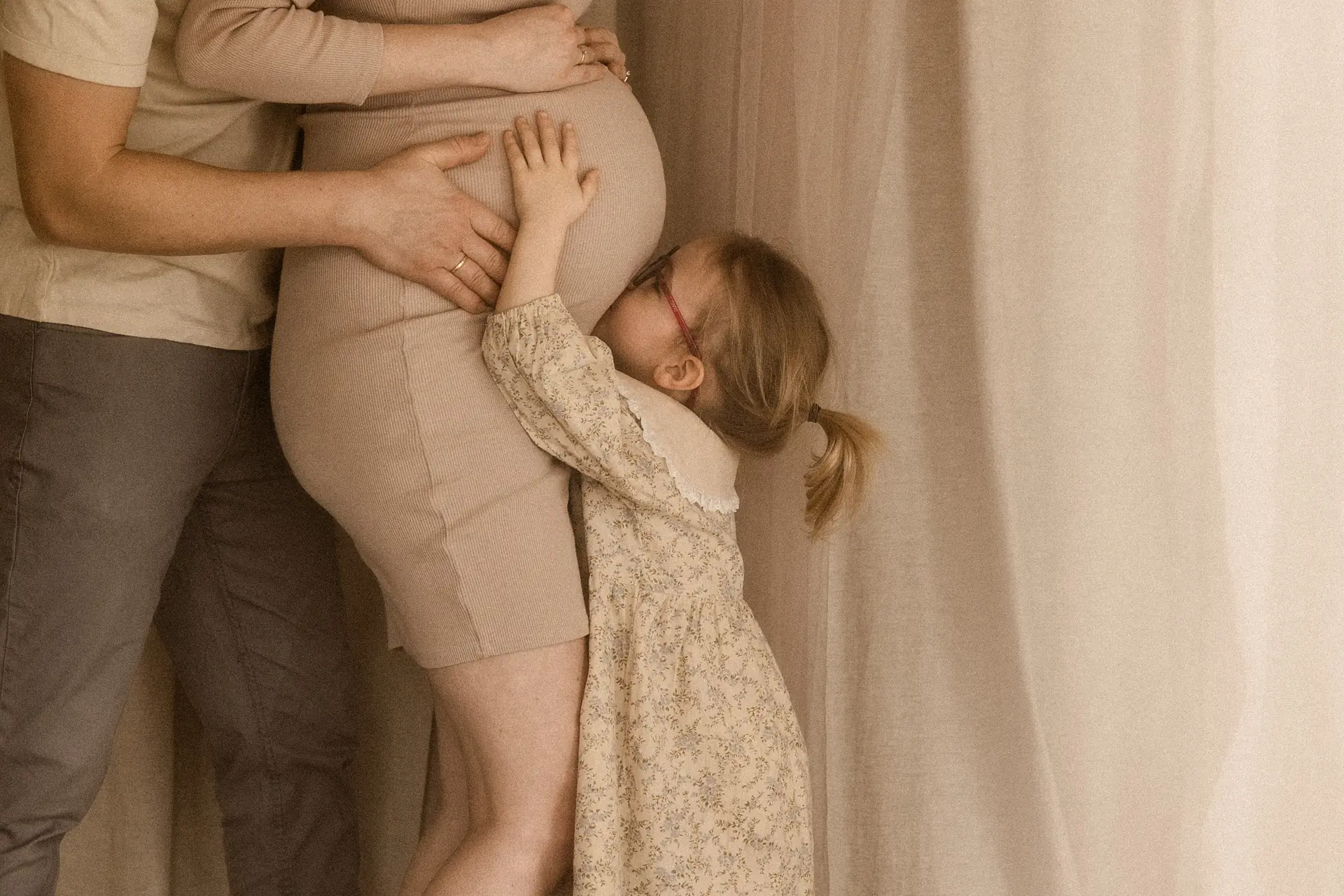 Starsza córeczka przytula i całuje brzuszek mamy podczas naturalnej sesji ciążowej