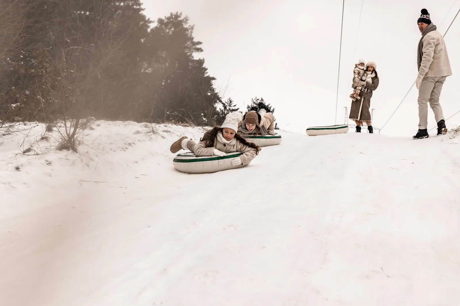 Wyścigi dzieci kto pierwszy zjedzie z górki śnieżnej na kołach dmuchanych podczas sesji plenerowej w stylu filmowym