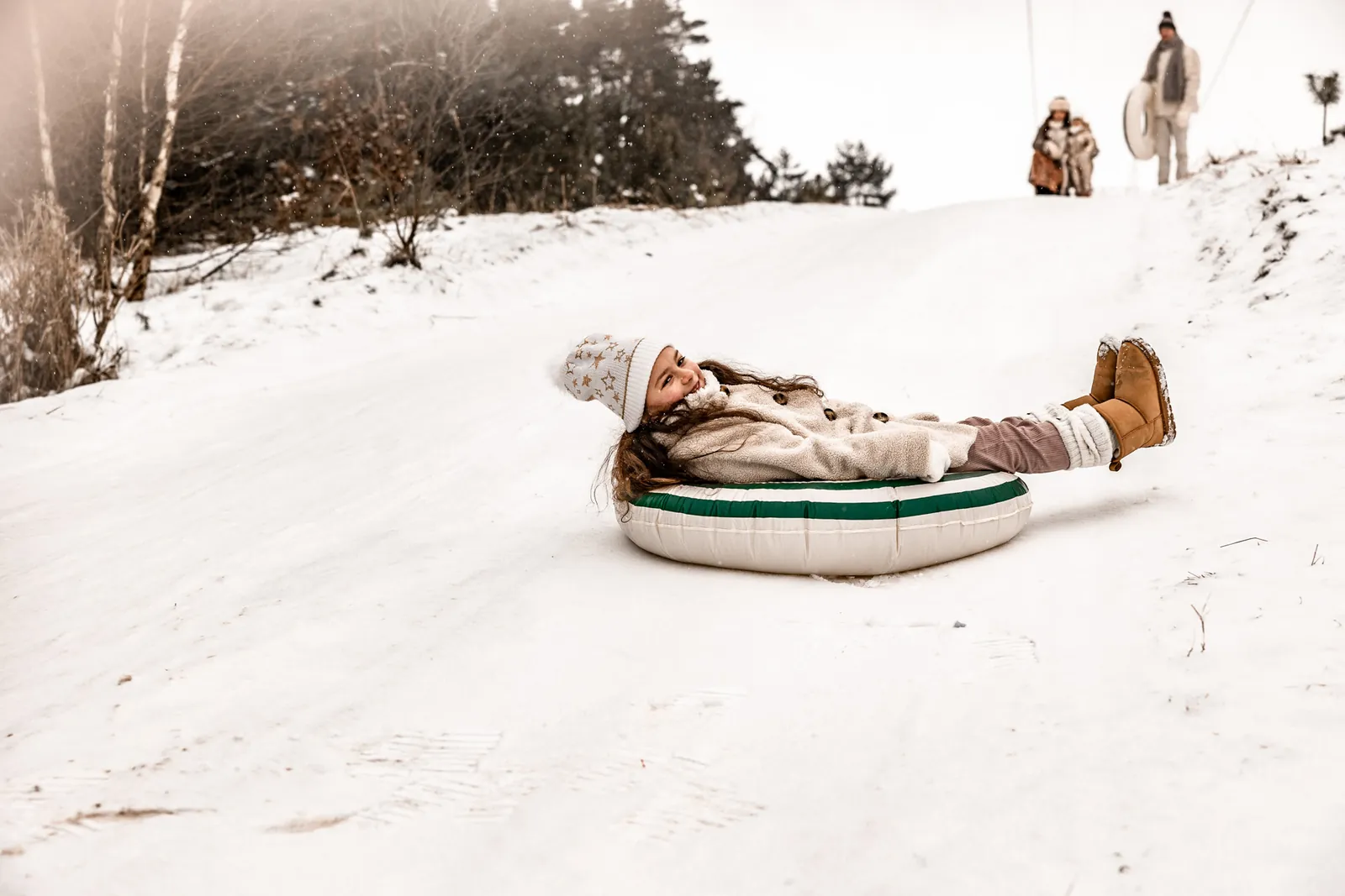 Dziewczynka zjeżdża z górki na dmuchanym kole, w tle las i śnieg
