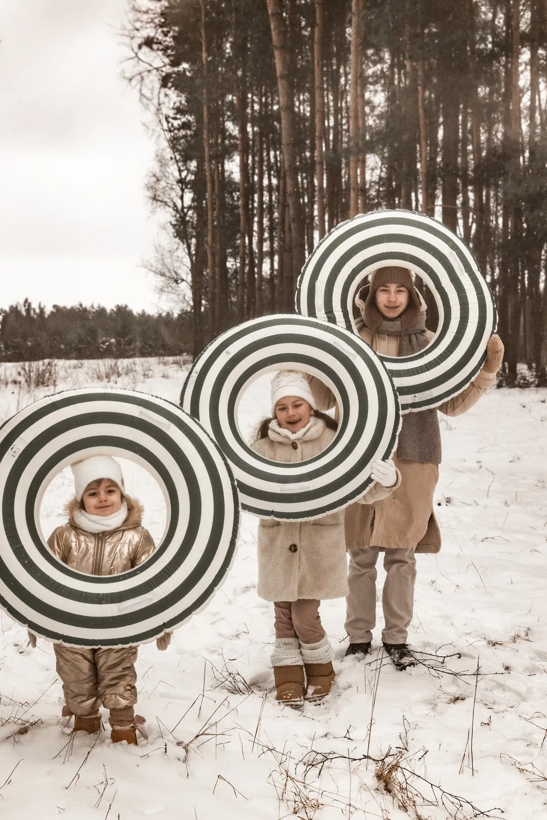 Trójka dzieci wygląda przez koła dmuchane na śnieg podczas zimowej sesji zdjęciowej w śnieżnym plenerze